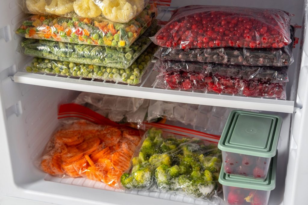 Bags and boxes of frozen vegetables and berries stacked on the shelves of a freezer