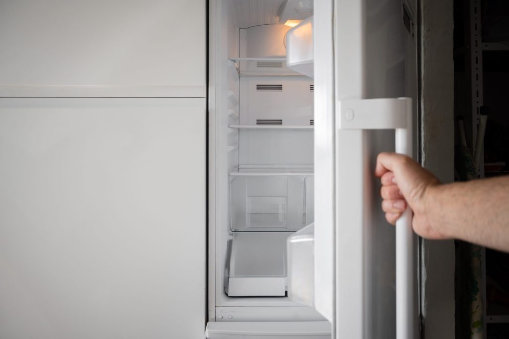 A hand pulling open a refrigerator door, the edge of the door and its seal in view