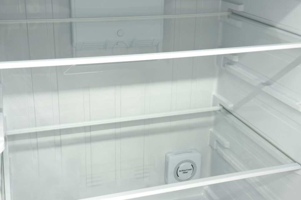 The interior of an empty refrigerator, glass shelves and the plain back wall behind them
