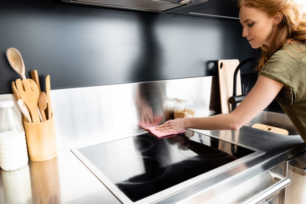A hand wiping down a black ceramic cooktop with a cloth