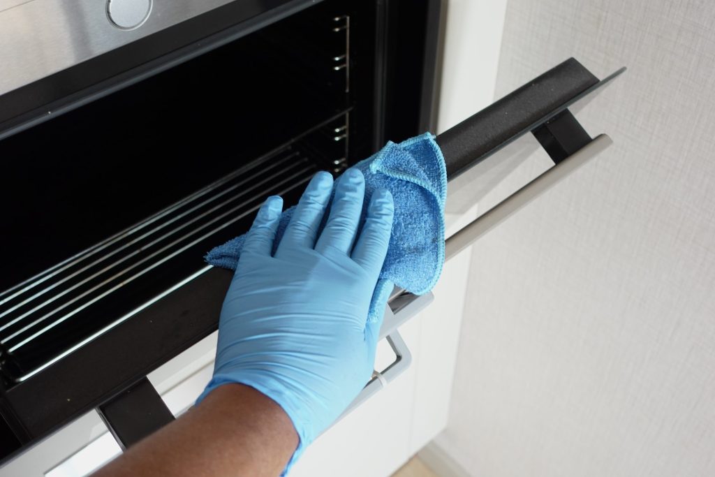 A gloved hand cleaning the inside of an oven with a microfiber cloth