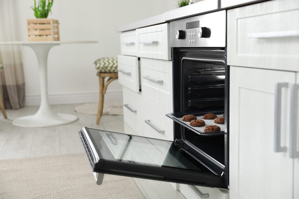 A tray of baked cookies on the open door of a wall oven in a white kitchen