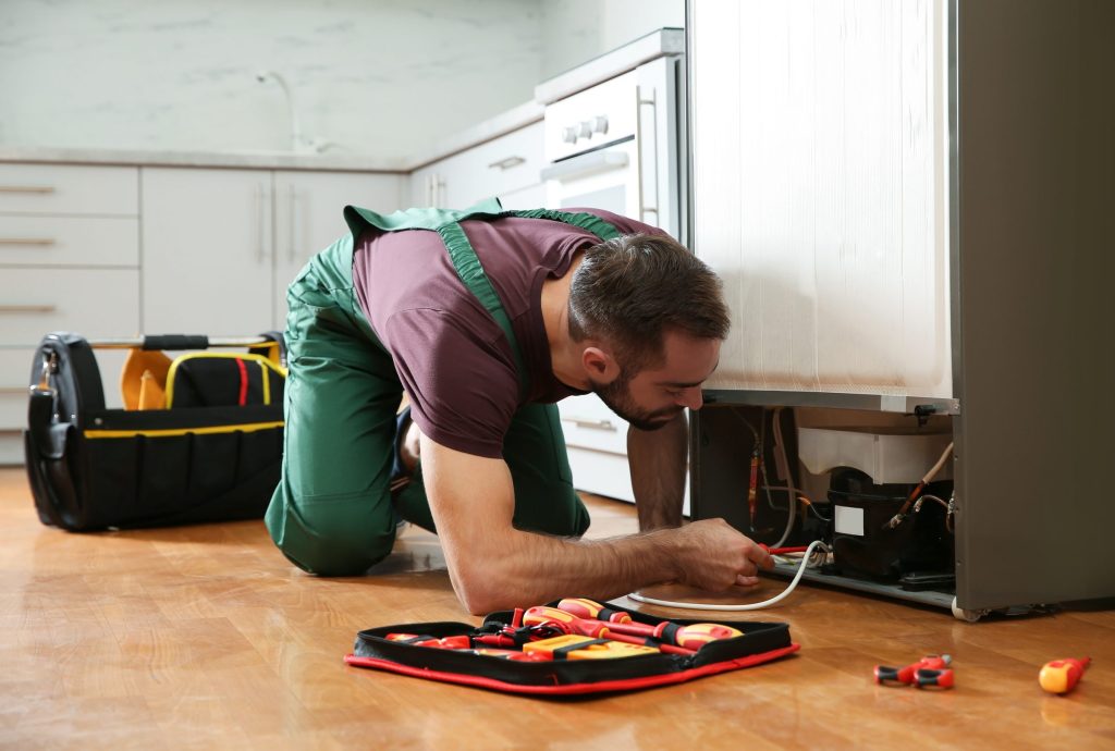 A technician working behind a refrigerator with his tool roll laid out on the floor