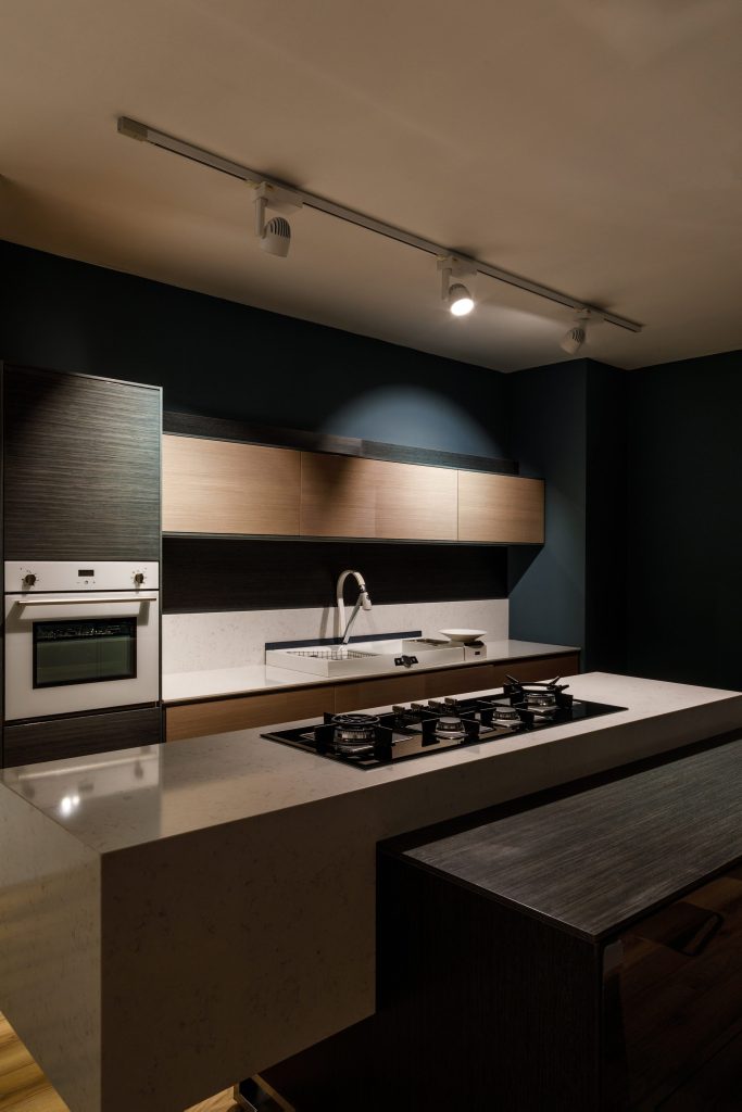 A gas cooktop set into a stone island in a dark blue kitchen with an oven column