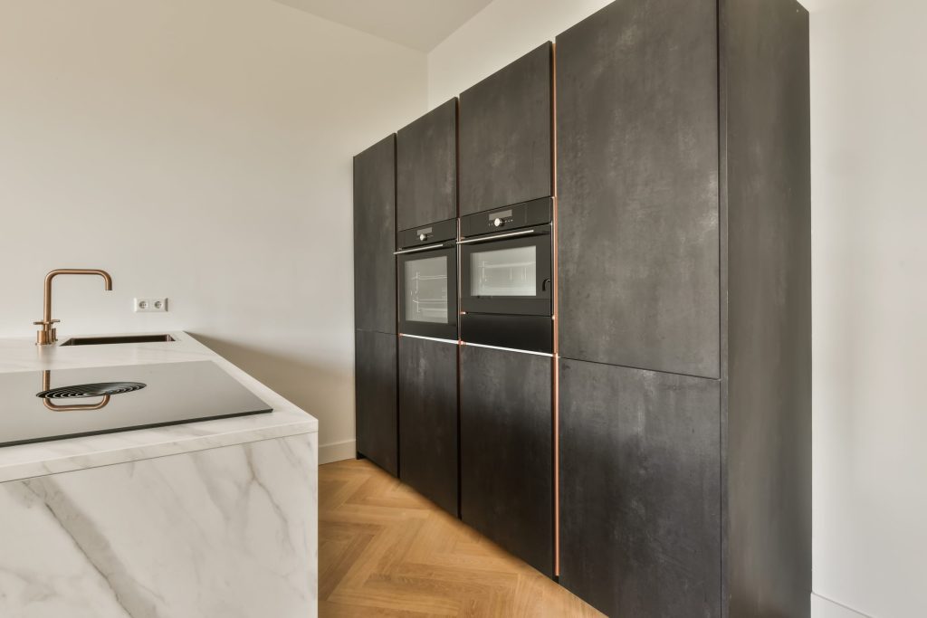 A dark tall cabinet run with two built-in ovens, copper reveals and a marble island