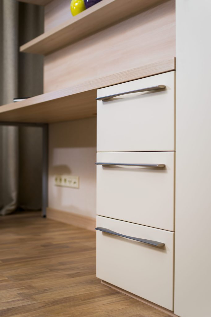 Pale cabinet drawer fronts with long metal handles, close up