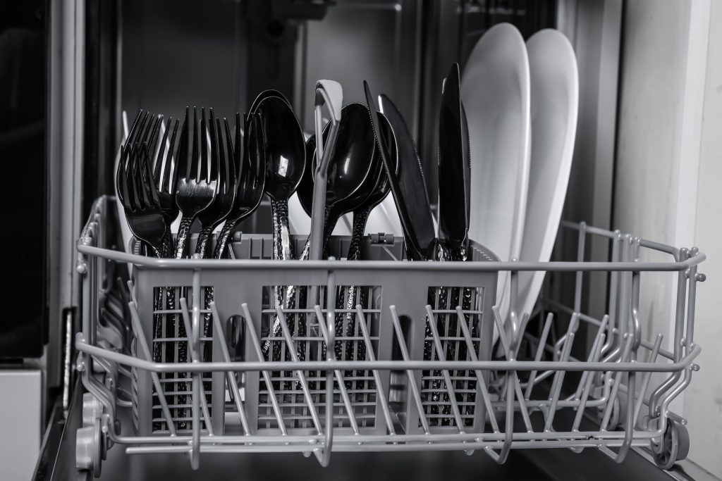 A cutlery basket full of clean forks and spoons in a dishwasher