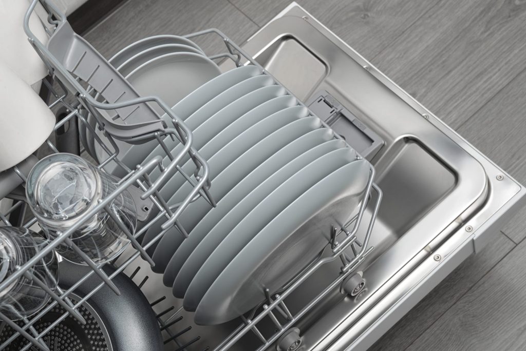 The lower rack of a dishwasher pulled out, loaded with plates and a pan
