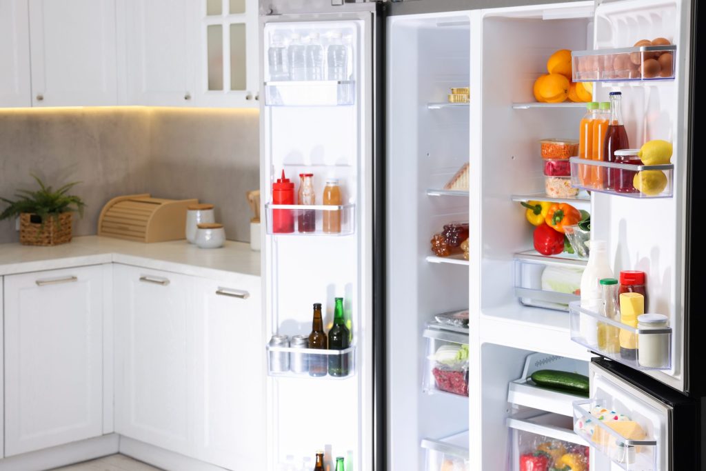 A tall refrigerator standing open on both doors, shelves and racks fully stocked