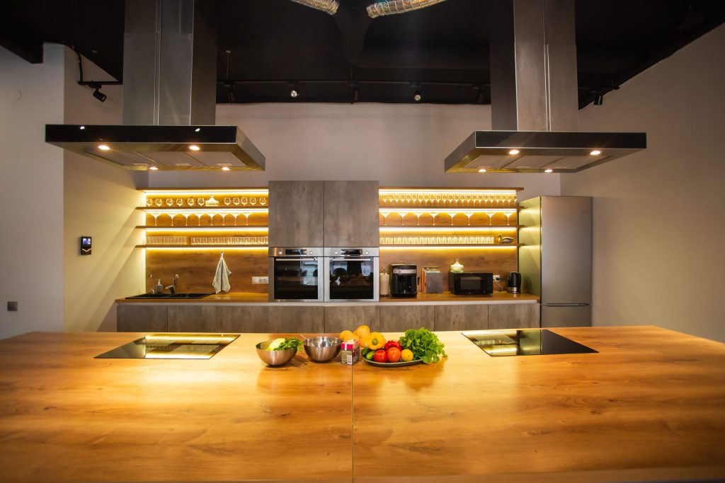 A long oak island under two hoods, with wall ovens set into a lit run behind