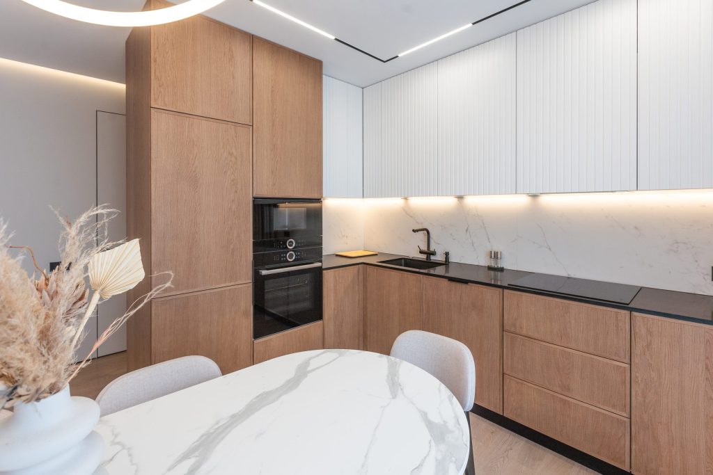 An oak and white kitchen run with a built-in oven, beside a marble dining table