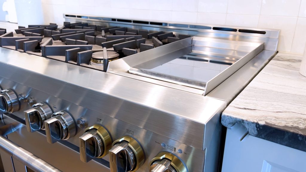 A stainless professional rangetop with sealed burners, a griddle plate and heavy brass-collared knobs