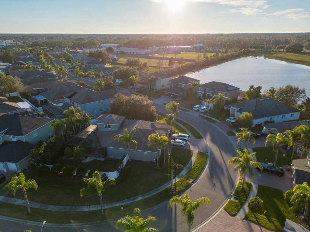 An aerial view of a suburban cul-de-sac of tile-roofed houses beside a lake at sunset
