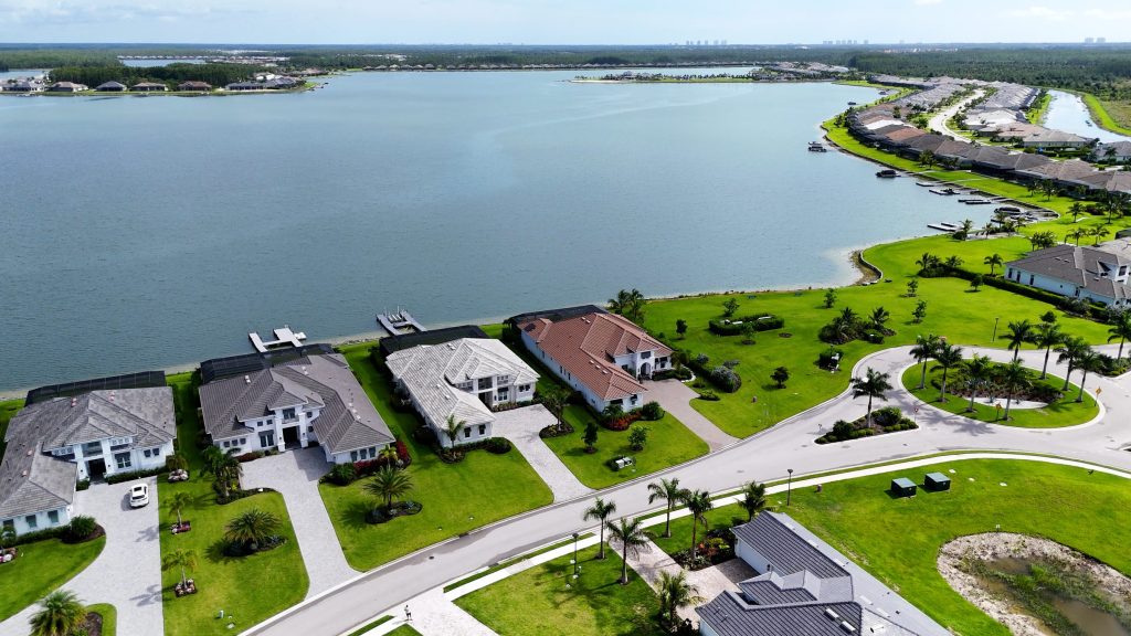An aerial view of large houses along the edge of a wide lake, palms and lawns between them