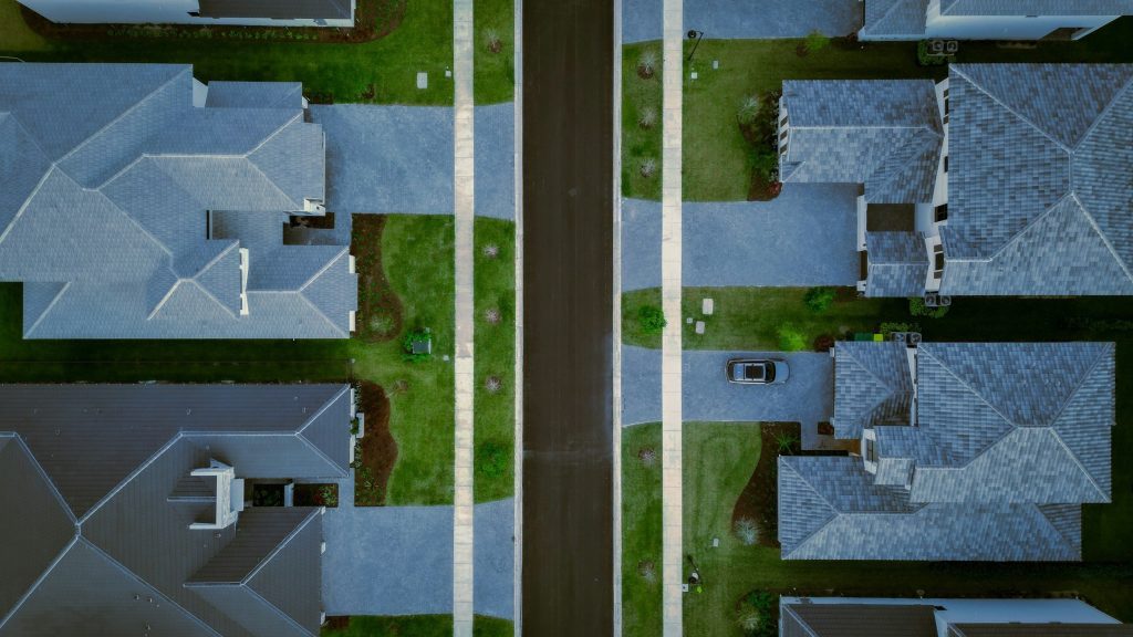 An overhead view of a residential street, shingle roofs and lawns on both sides of the road