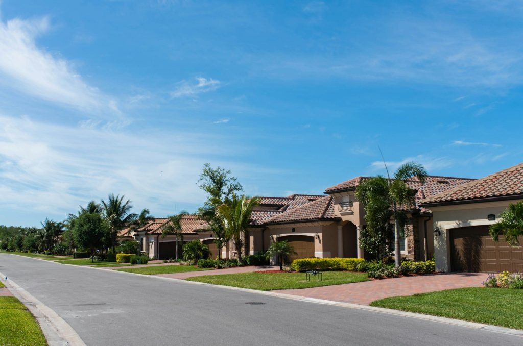 A quiet suburban street lined with houses, palm trees, and manicured lawns