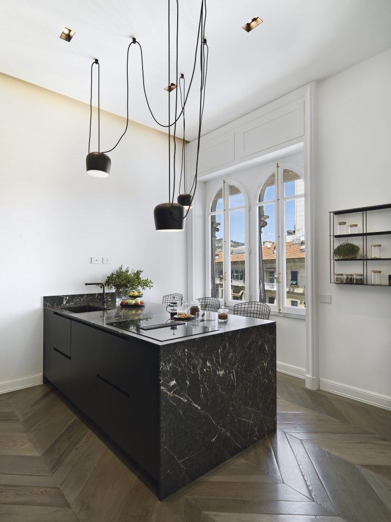 A black marble island under sculptural pendants in a pale room
