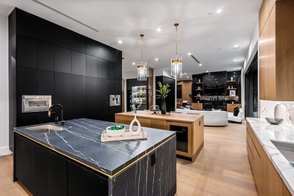 A black marble island with a gold edge in an open-plan kitchen with a dark panelled wall
