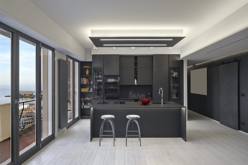 A total-black kitchen in a high-rise, an island with two stools and a wall of glass onto the ocean