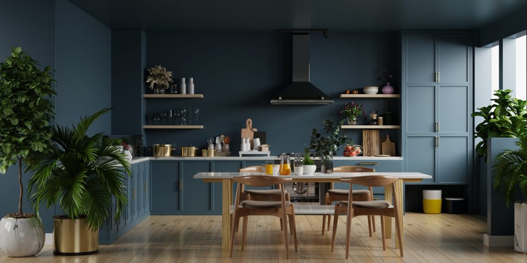 A deep blue kitchen with white worktops, a wooden table and large plants