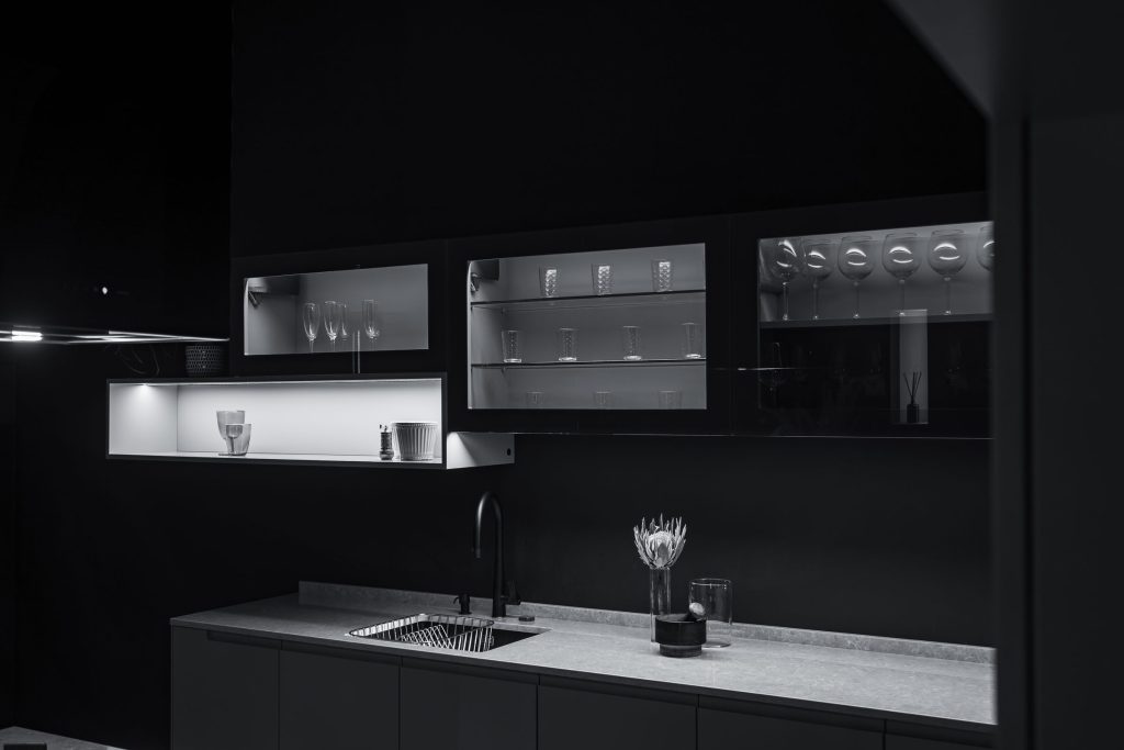 A dimly lit minimalist kitchen, a stone worktop and lit glass-fronted wall units