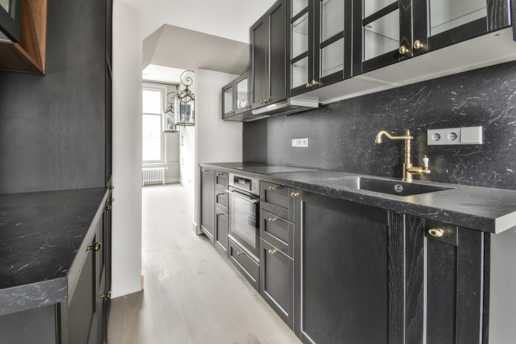 A dark stone kitchen run with a brass tap and glass-fronted cabinets