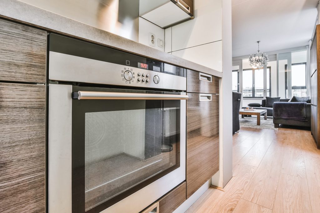 A stainless wall oven in wood cabinetry, with the living room beyond