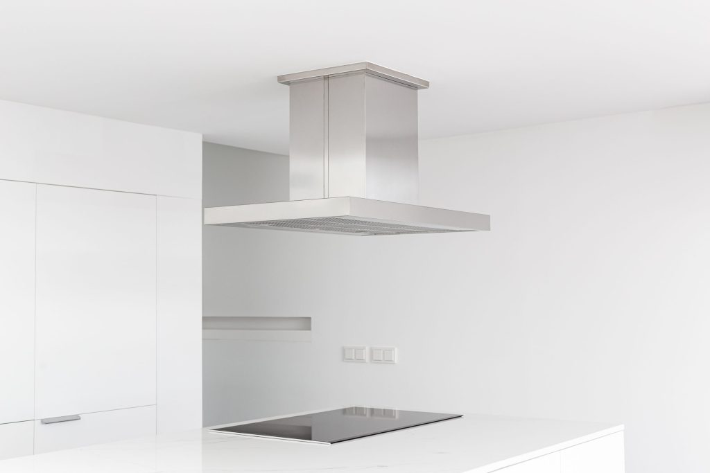 A minimal white kitchen with a stainless island hood above a flush induction cooktop