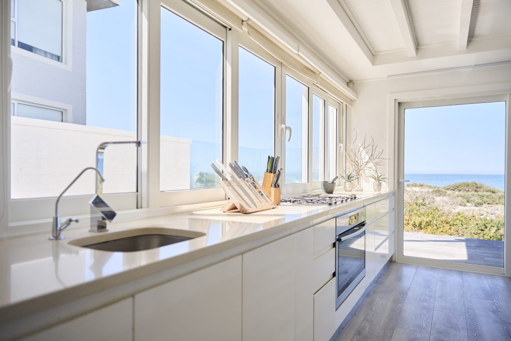A white kitchen run under a window band looking out to the sea