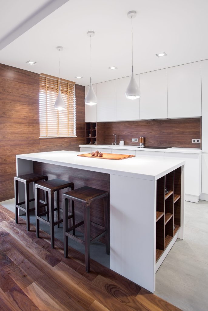 A white kitchen island with open walnut shelving under a walnut splashback