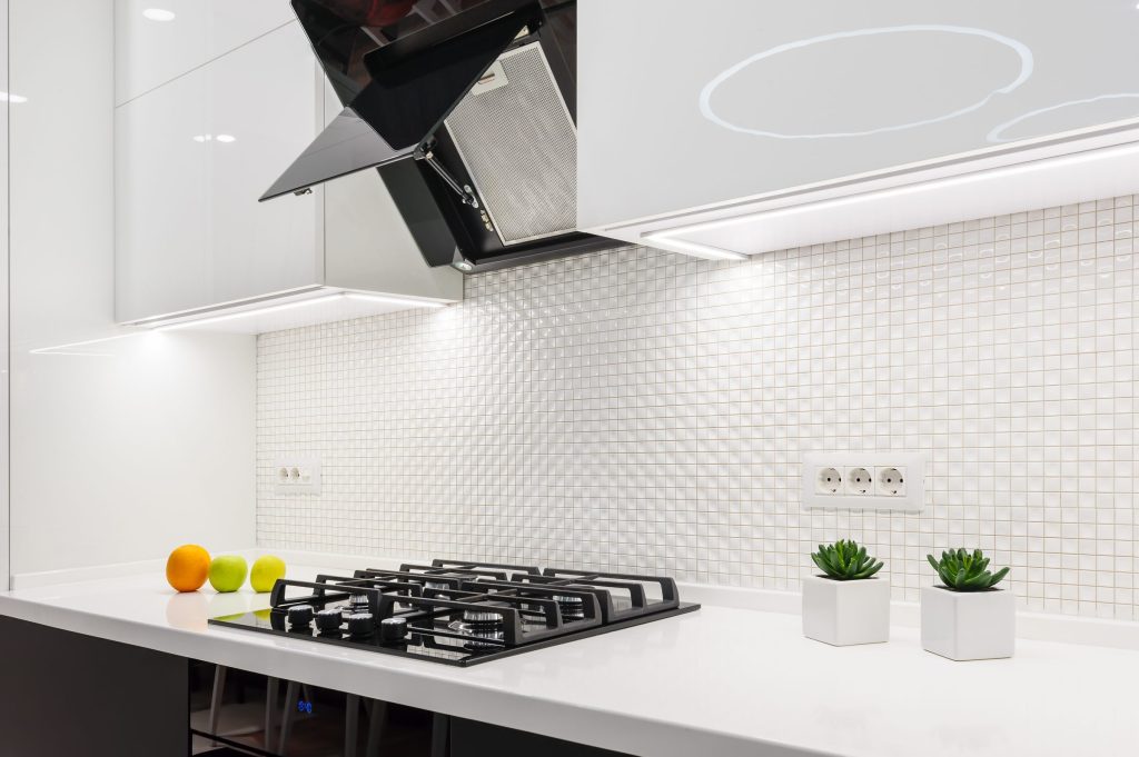 A white kitchen with a mosaic splashback, angled hood and a gas cooktop
