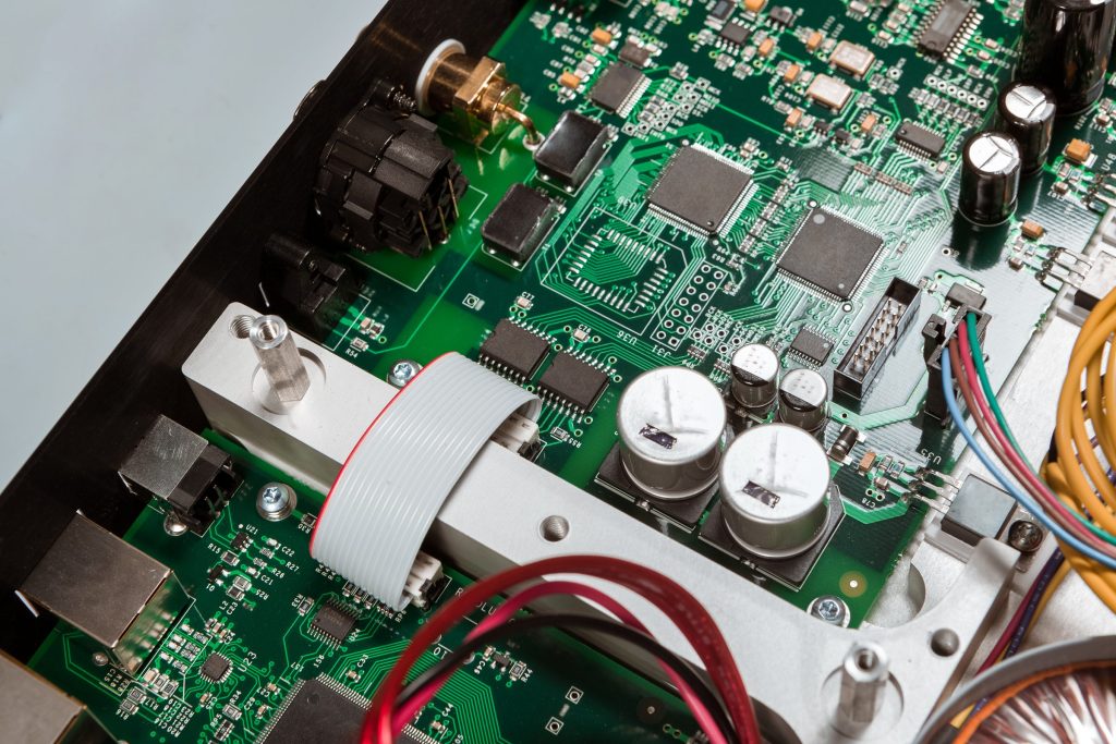 A green circuit board with its capacitors and ribbon cable, close up