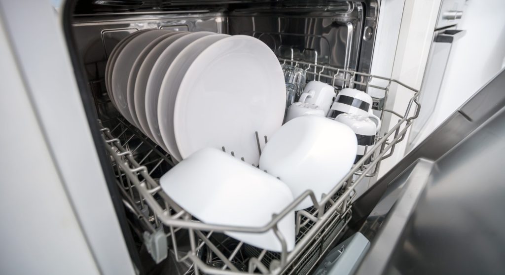 The upper rack of an open dishwasher holding clean plates and cups