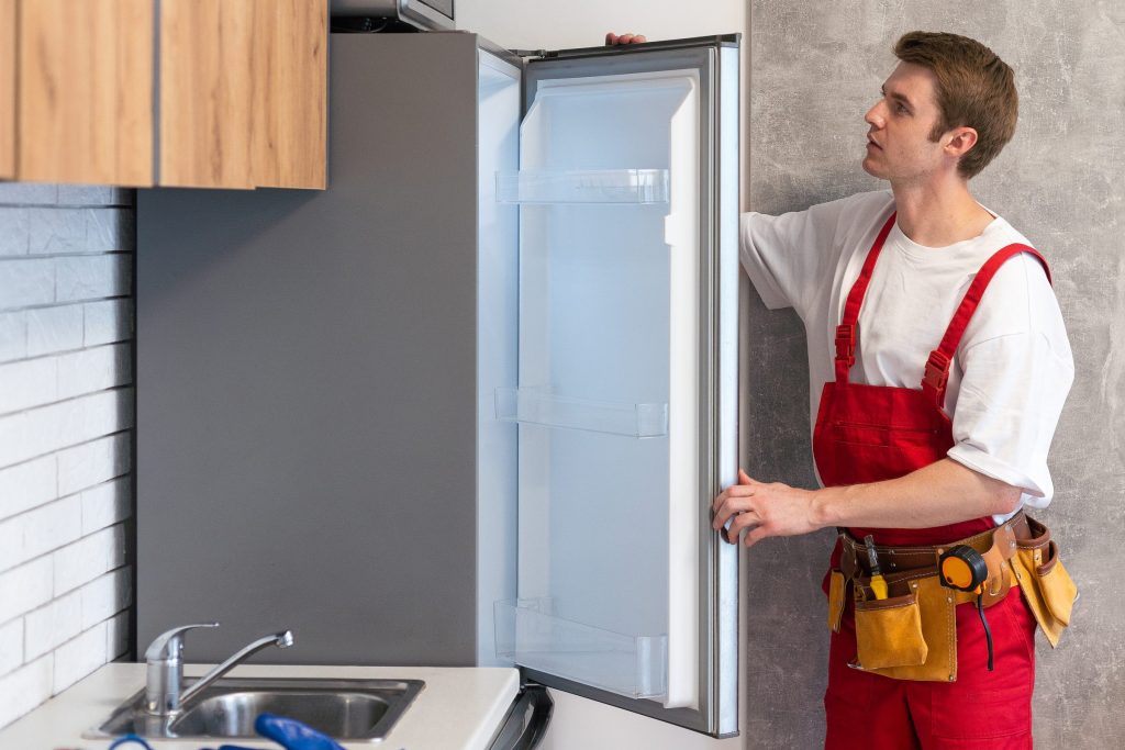 A technician holding the open door of a built-in refrigerator, tool belt at his waist