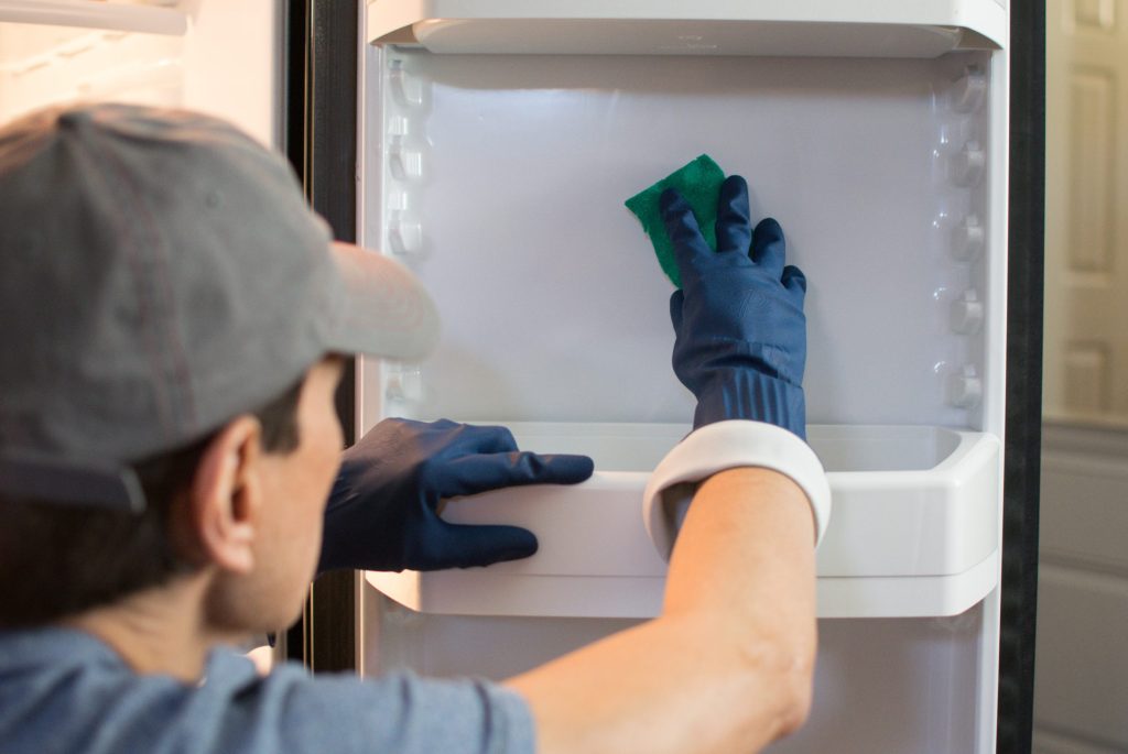 A gloved hand wiping the door shelf of an open refrigerator