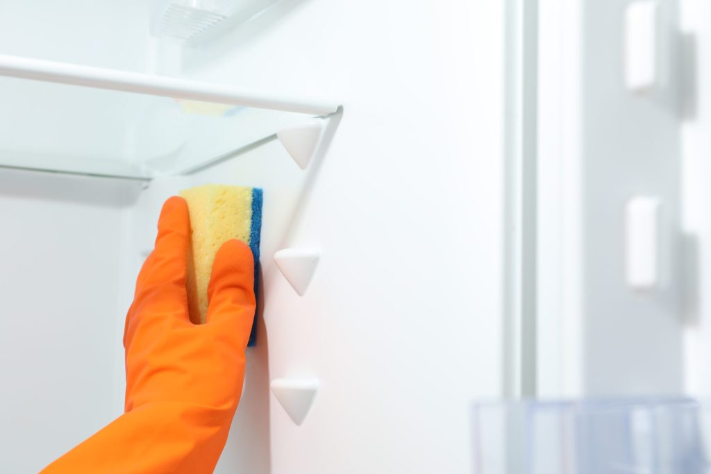 A gloved hand with a sponge cleaning the shelf brackets inside an empty refrigerator