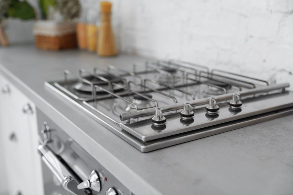 A stainless gas cooktop set into a light stone counter