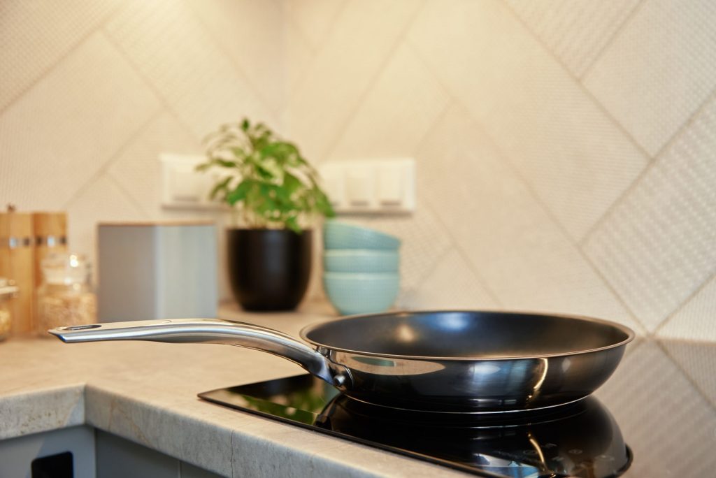 A frying pan resting on the black glass surface of a cooktop