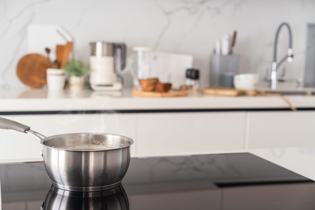 A steel saucepan steaming on a black induction cooktop in a bright kitchen