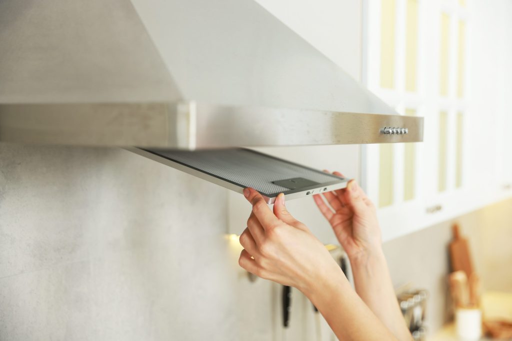 Two hands lifting the metal grease filter out of a range hood