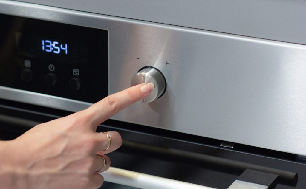 A finger pressing the control beside the lit display of a stainless wall oven