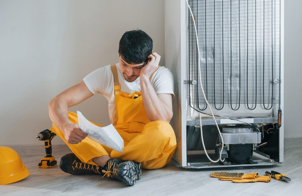 The condenser coils on the back of a refrigerator, with a technician reading beside it
