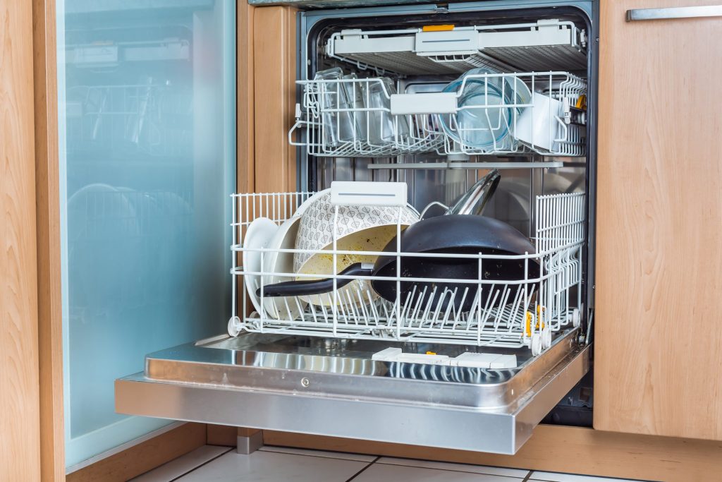 An integrated dishwasher, its door down, loaded with unwashed pans and plates