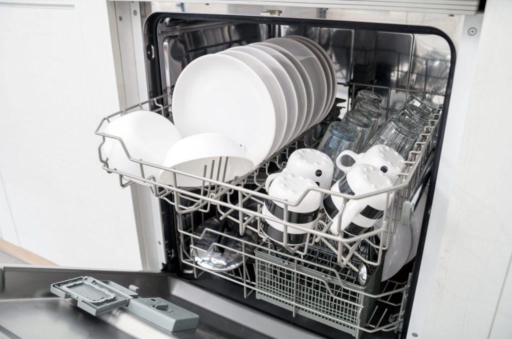 A dishwasher standing open with a full load of white crockery