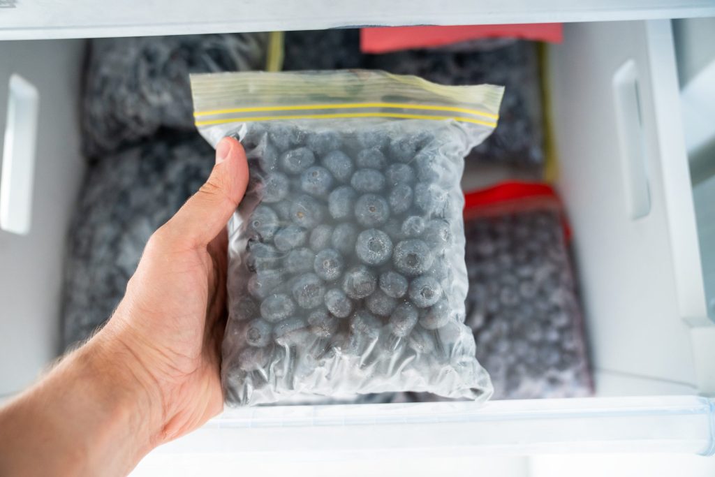 A hand holding a bag of frozen blueberries taken from a freezer drawer