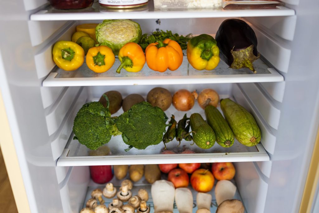 Shelves of peppers, broccoli and root vegetables inside a refrigerator