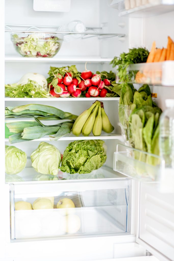 A tall refrigerator standing open, its shelves stocked with salad and vegetables