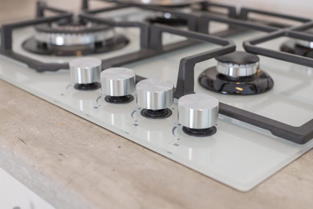 A white gas cooktop with black grates and heavy steel knobs