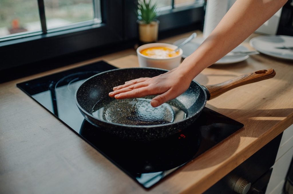 A hand held over a frying pan standing on a black induction cooktop
