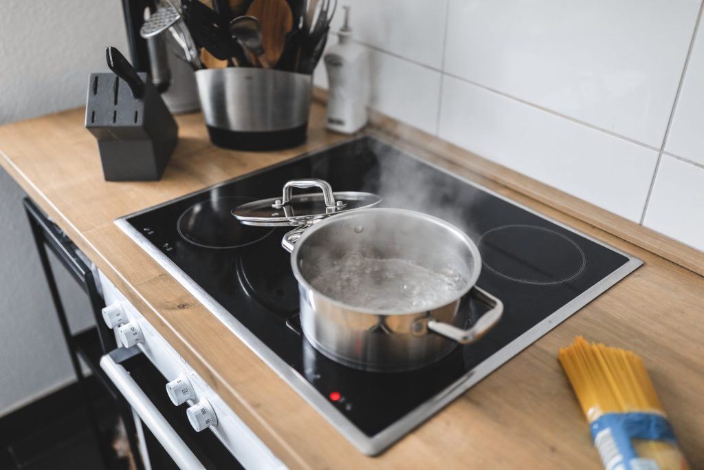 A steel pot boiling on a black cooktop set into a wooden worktop